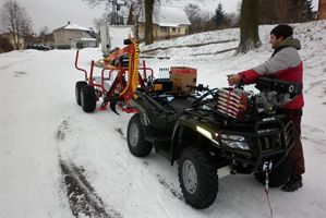 Muž u čtyřkolky s vyvážecím přívěsem Kranman na zasněžené cestě