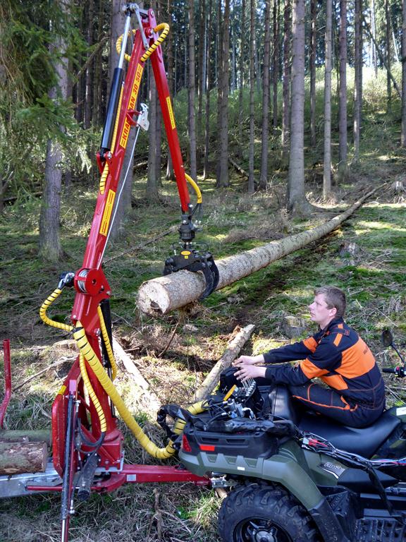 Obsluha čtyřkolky ovládá hydraulickou ruku přívěsu Kranman při nakládání kmene