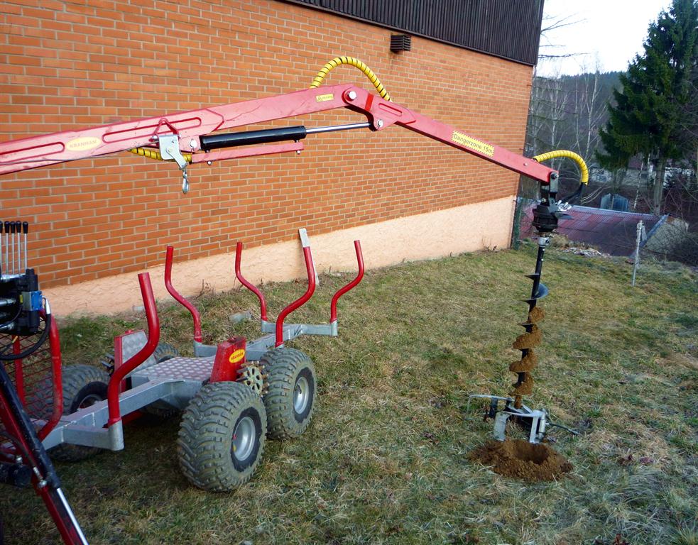 Přívěs Kranman s hydraulickou rukou a zemním vrtákem při vrtání do země