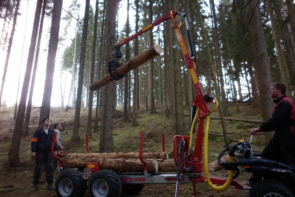 Vyvážecí přívěs Kranman s hydraulickou rukou nakládá kmen v lese, obsluha vedle stroje