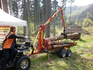 Obsluha čtyřkolky nakládá dřevo na přívěs Kranman s hydraulickou rukou na akci v lese